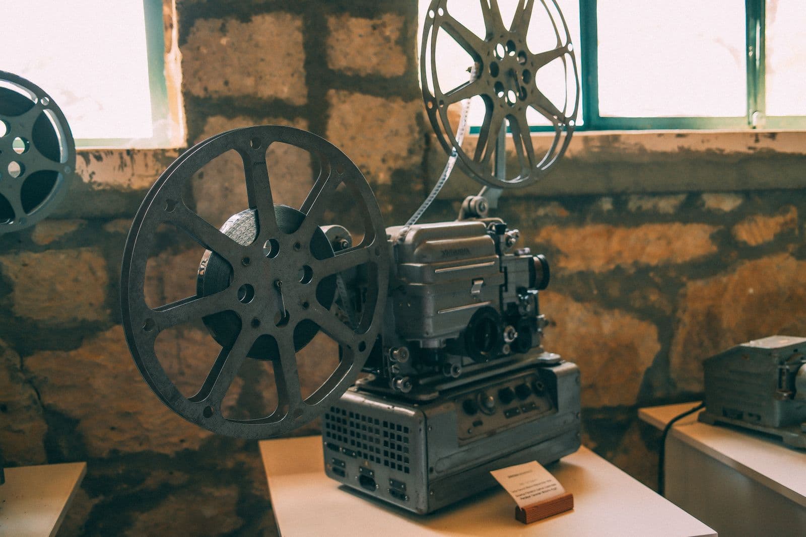 Zabytkowy projektor filmowy ustawiony we wnętrzu o surowym, rustykalnym charakterze